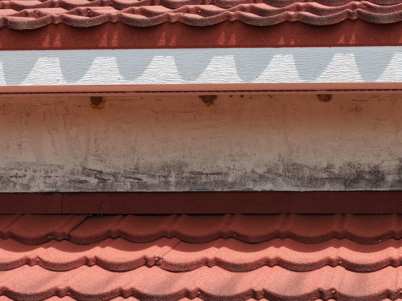 Close drone view of a band board beneath a roof eave with mildew growth along its lower edge