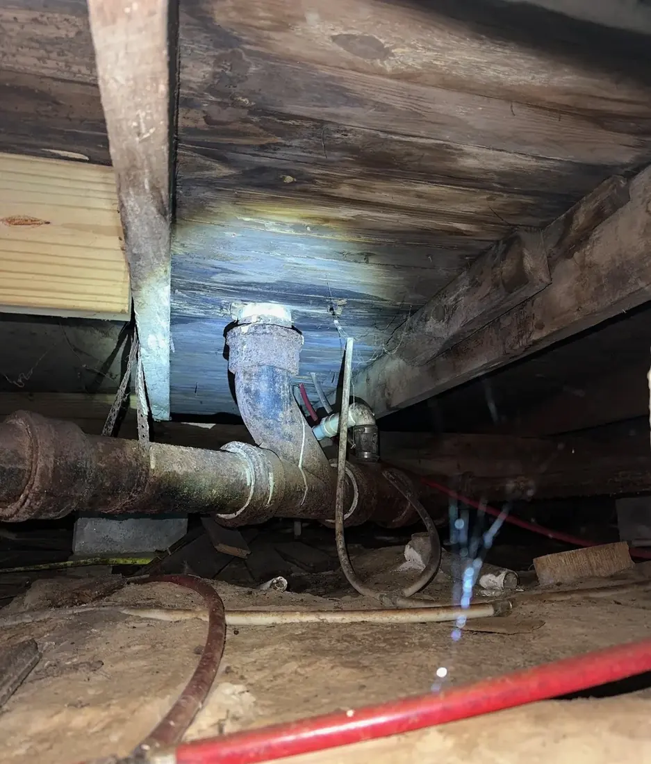 Heavily rusted cast iron drain piping running through a crawl space beneath floor joists