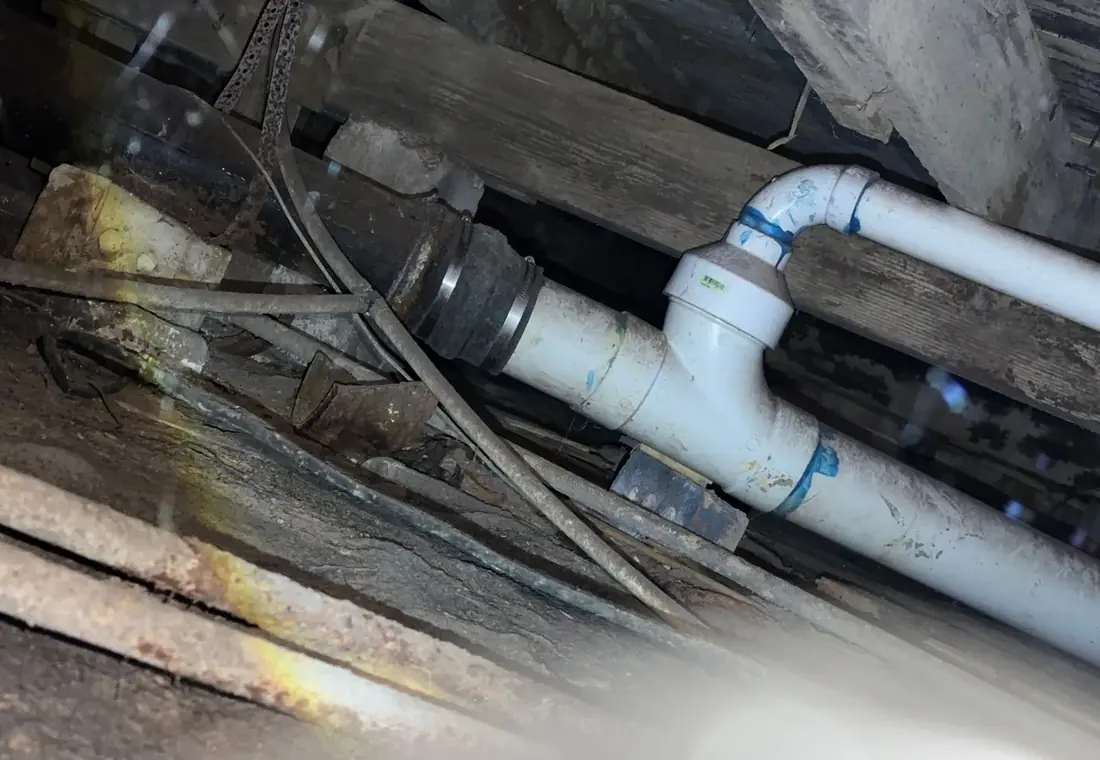 A rubber coupling joining new white PVC drain pipe to old cast iron pipe in a crawl space