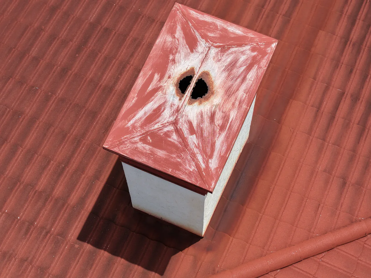 Close overhead view of a metal chimney chase cover with a large rusted-through hole at the centre seam