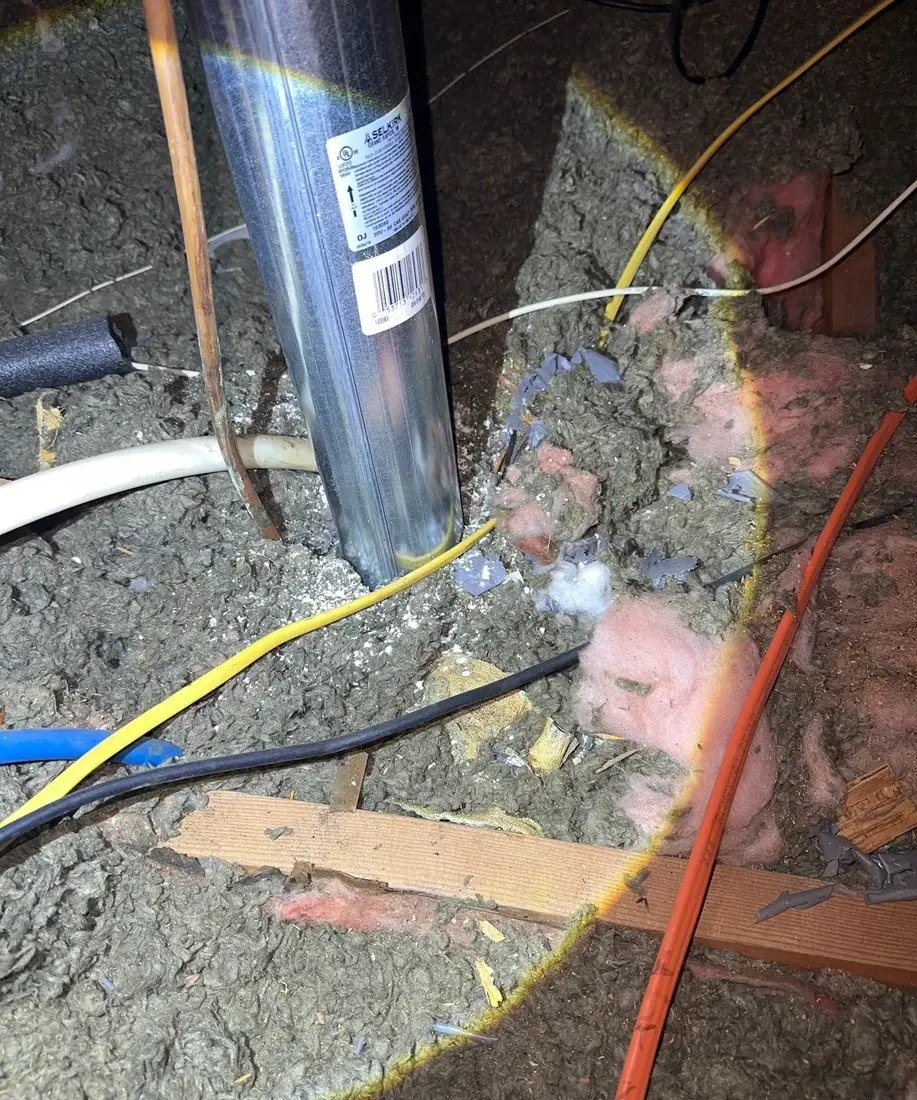 A metal flue pipe passing through attic floor insulation with loose insulation packed around it