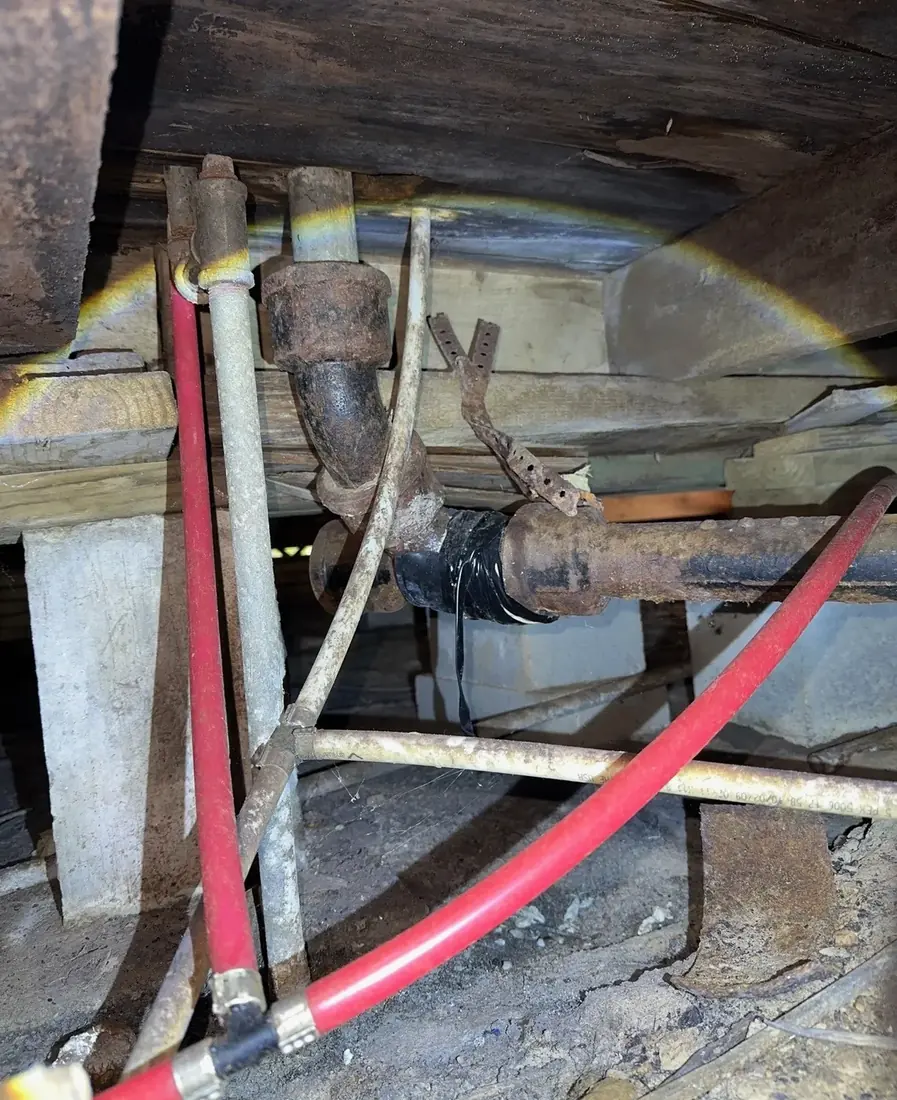 Corroded steel water piping in a crawl space next to newer red and white PEX lines
