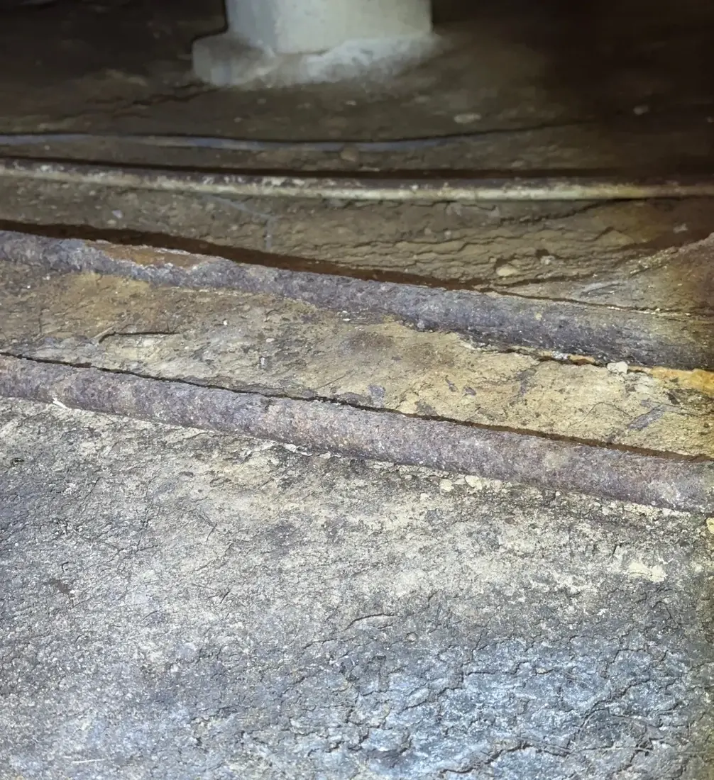 A rusted galvanized steel water pipe lying on bare soil in a crawl space