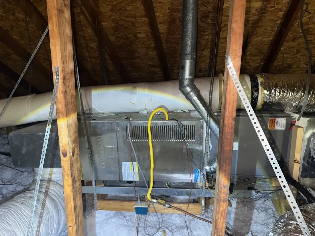 An HVAC air handler mounted on a platform in an attic with supply ducts, flue and a yellow gas line connected