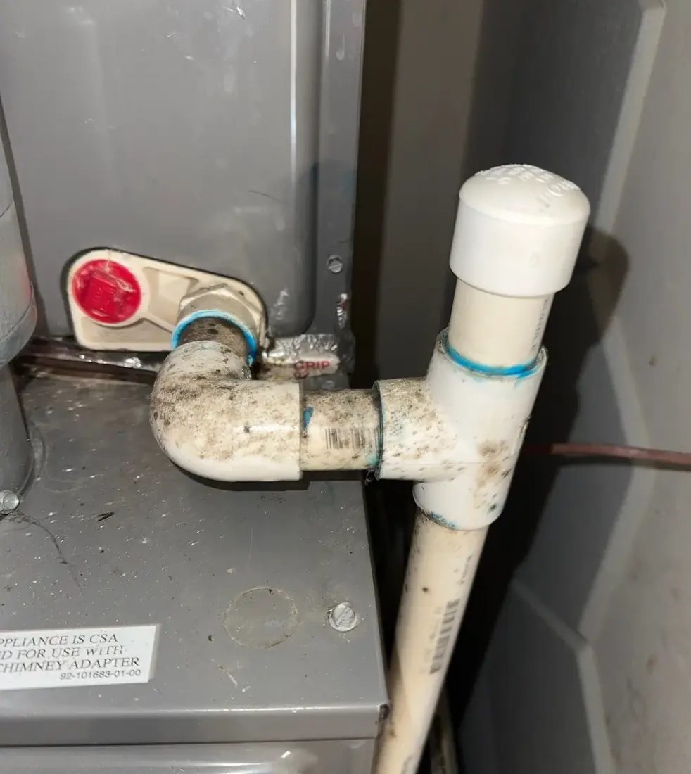 PVC condensate drain piping with a capped cleanout tee at the side of a furnace