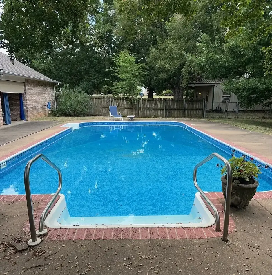 A rectangular vinyl-liner in-ground swimming pool in an East Texas backyard with clear blue water, handrails and a diving board