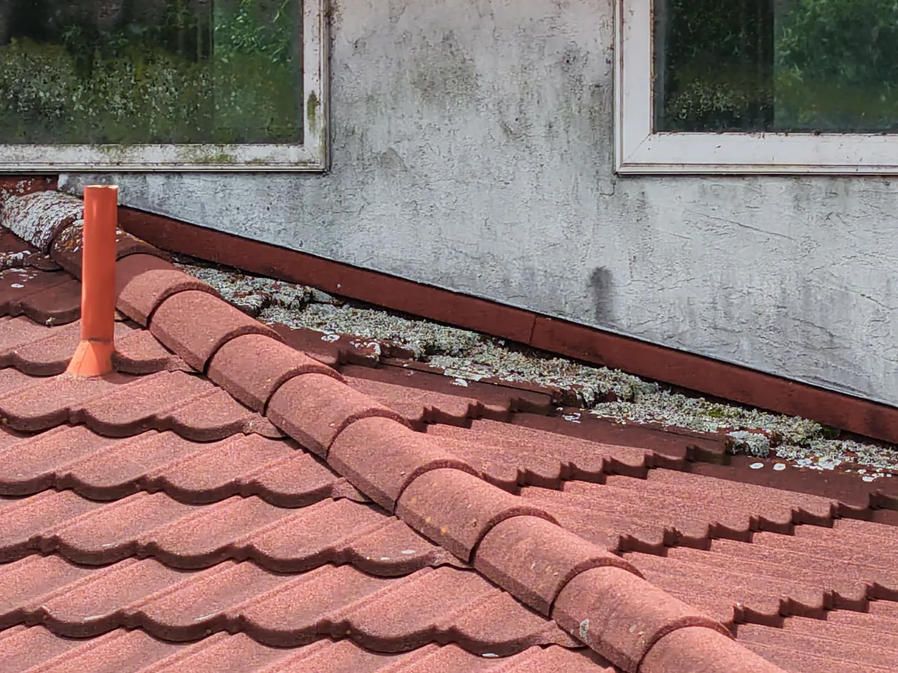Drone view of a roof-to-wall transition on a metal tile-profile roof with debris and organic growth accumulated in the channel along the wall
