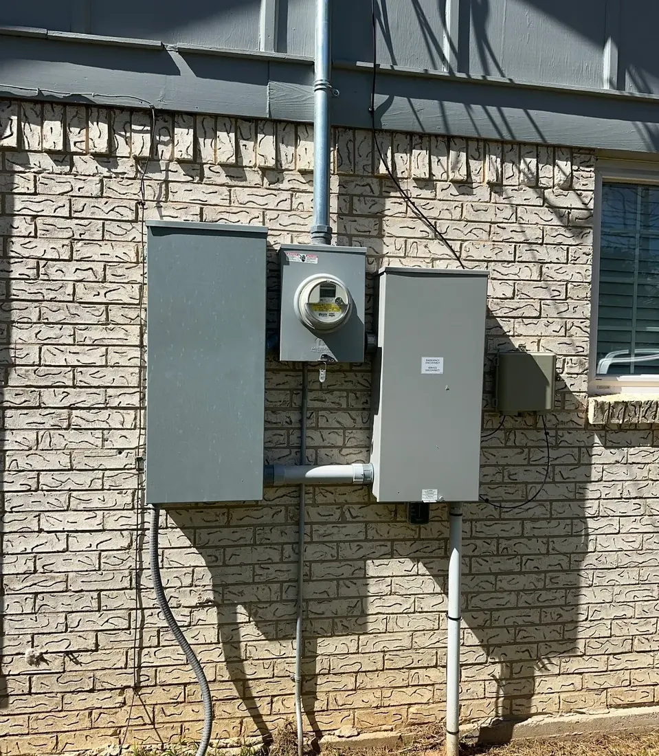 Exterior brick wall with an electrical meter, service disconnect enclosure and main panel installed side by side