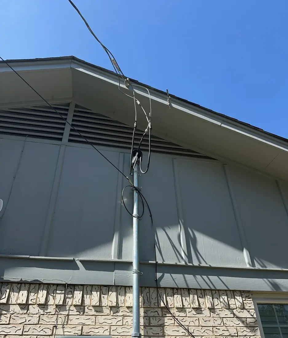 An electrical service mast with overhead service drop conductors connecting to the side of a house