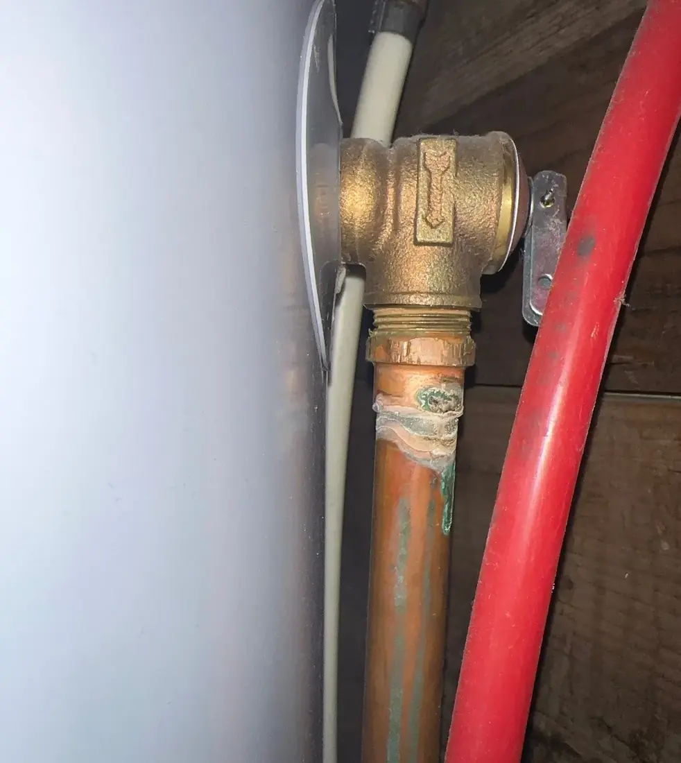 A brass temperature and pressure relief valve on a water heater with a copper discharge line showing green corrosion staining below it