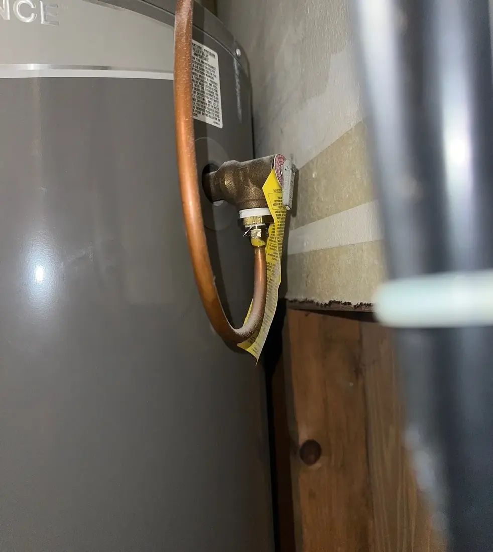A water heater temperature and pressure relief valve with a copper discharge pipe and the original yellow warning tag still attached