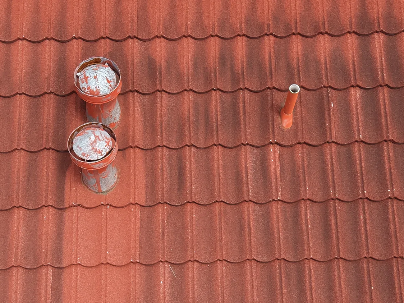Overhead drone view of two plumbing vent collars on a red metal roof that have been sealed with mastic and painted to match