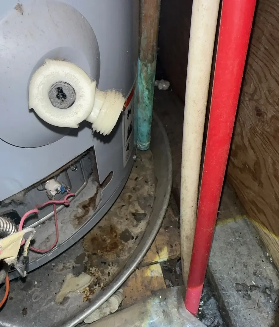 A plastic water heater drain valve with rust staining in the drip pan beneath it