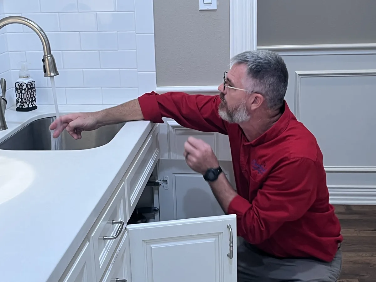 Jeff Stalnaker running a kitchen faucet while watching the cabinet below for leaks