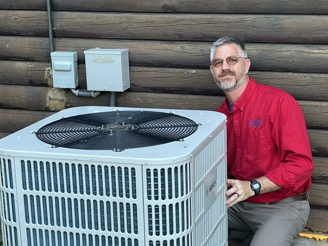 Jeff Stalnaker kneeling beside an outdoor air conditioning condenser during an inspection