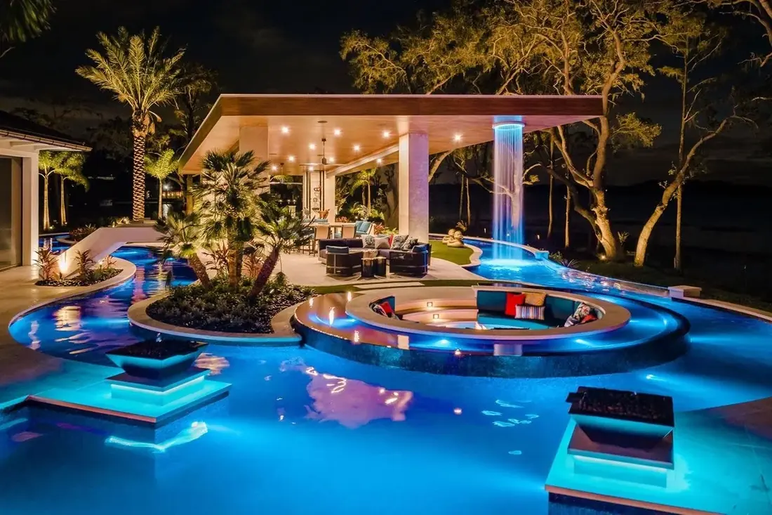 A residential pool at night with a covered pavilion, rain curtain water feature, sunken seating area and lit water — a Florida property Jeff Stalnaker worked on during his years in the pool equipment industry.